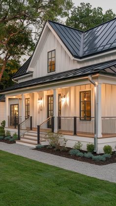 a white house with black metal roof and porch railings on the front lawn at dusk