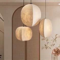 three lamps hanging from the ceiling above a table with flowers and vases on it