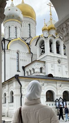 a person standing in front of a large white building with gold domes on it's sides