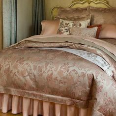 a bed with pink and gold comforters in a bedroom next to a curtained window