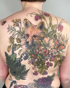 the back of a woman's body with flowers and a fox tattoo on it