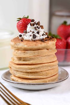 a stack of pancakes topped with whipped cream and chocolate chips on a plate next to strawberries