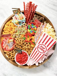 a wooden bowl filled with candy, pretzels, popcorn, and other snacks