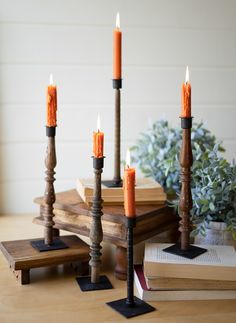 an assortment of candles sitting on top of a wooden table next to books and plants