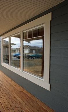 an empty porch with wooden floors and large windows on the side of a house, overlooking a parking lot