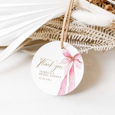 a thank you tag with a pink bow on it sitting next to feathers and flowers