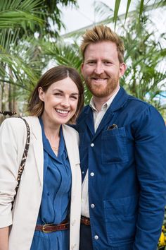 a man and woman standing next to each other smiling at the camera with palm trees in the background