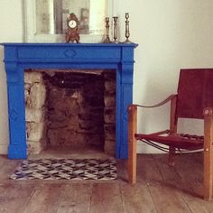 a living room with a blue fireplace and wooden chair next to an old fashioned mirror on the wall