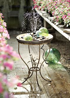 an outdoor table with water spewing out of it's top and flowers in the background