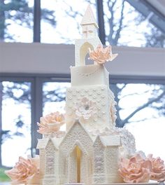 a white wedding cake with pink flowers and a church in the middle on a table