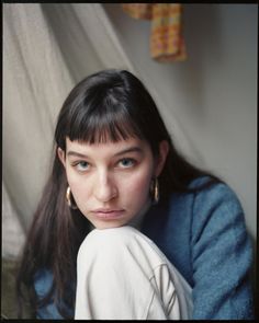 a woman with long black hair and blue eyes is posing for a photo in front of a curtain