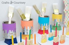 some toothbrushes are sitting in tins on a table with colorful paint brushes