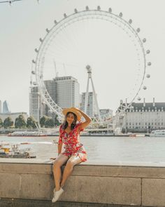 a woman in a red dress and straw hat sitting on a wall next to the water