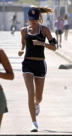 a woman running down the street in shorts and a tank top with her hat on