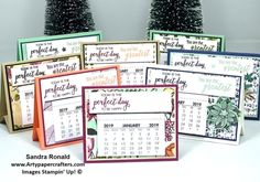 several calendars are sitting next to each other on a table with christmas trees in the background