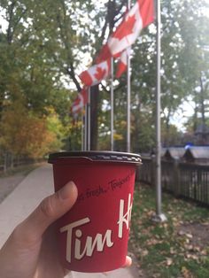 a person holding up a red cup with the word tink on it in front of canadian flags