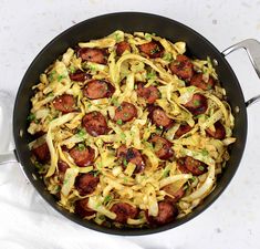 a skillet filled with sausage and noodles on top of a white tablecloth next to a fork