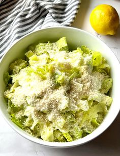 a white bowl filled with lettuce and cheese next to a lemon on a table