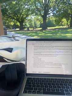 an open laptop computer sitting on top of a wooden table next to a park filled with trees