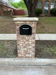 a brick mailbox sitting on the side of a sidewalk next to a tree and grass