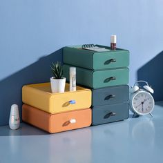 three different colored boxes stacked on top of each other next to an alarm clock and air freshener dispenser