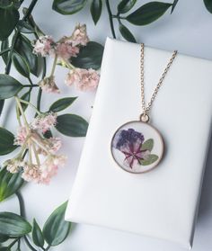 Embrace the timeless charm of nature with this exquisite necklace, featuring real dried pressed flowers lovingly preserved in crystal-clear resin. 🌿✨  Each flower is carefully selected and arranged to create a unique, one-of-a-kind piece that captures the essence of a blooming garden. 🌼🌺  This necklace is perfect for adding a touch of natural elegance to your everyday look or as a special gift for someone who cherishes the beauty of nature. 🎁💕  Handcrafted with love, it's more than just jew Botanical Birth Flower Round Pendant Necklaces, Botanical Flower Jewelry With Pressed Flowers, Elegant Necklace With Pressed Flower Pendant, Elegant Pressed Flower Pendant Necklace, Elegant Pendant Flower Necklace With Pressed Flowers, Nature-inspired Flower Necklaces With Pressed Flowers, Elegant Pressed Flower Necklaces As A Gift For Her, Elegant Necklaces With Pressed Flowers For Her, Elegant Pressed Flowers Necklace As Gift For Her