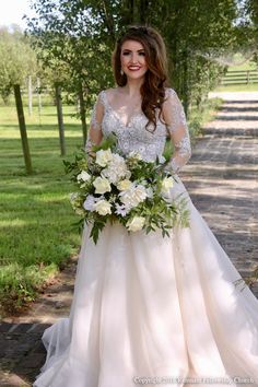 a woman in a wedding dress is holding a bouquet and smiling at the camera while standing on a path