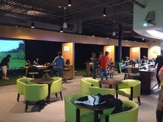 people standing and sitting at tables in an indoor golf club with large screens on the walls