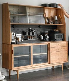 a woman standing next to a wooden cabinet filled with pots and pans on top of it