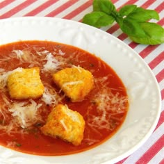 a white plate topped with soup and croutons on top of a red and white table cloth