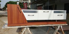 a white cabinet sitting on top of a piece of wood in front of a building