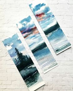 three watercolor paintings sitting on top of a white brick wall next to each other