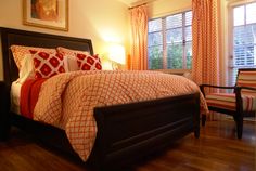 a bed sitting in a bedroom next to a window covered in orange and white curtains