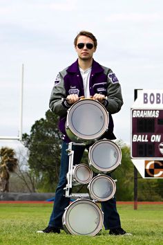 a man standing in the grass with some drums on his back and one hand behind him