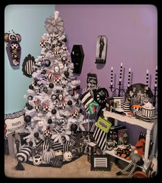 a white christmas tree with black and white decorations on it in front of a purple wall