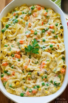 a casserole dish with noodles, peas and carrots in it on a wooden table