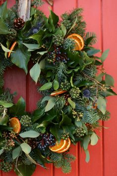 a wreath with oranges and greenery hanging on a red door, surrounded by pine cones