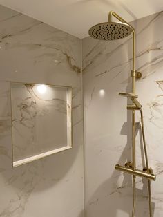 a bathroom with marble walls and flooring has a gold faucet shower head