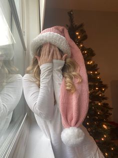 a woman wearing a pink hat and scarf covering her face next to a christmas tree