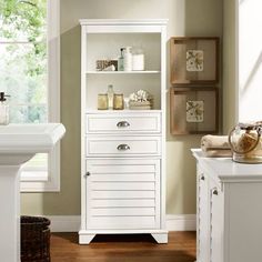 a white bathroom cabinet with drawers and shelves on the top, in front of a window