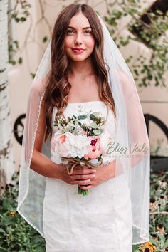 a woman in a white dress holding a bouquet of flowers and wearing a bridal veil