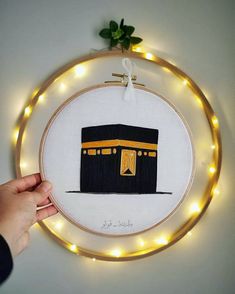 someone is holding up a cross stitched wall hanging with lights around it and there is a hand embroiderying pattern on the hoop