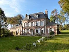 a large brick house sitting in the middle of a lush green field next to trees