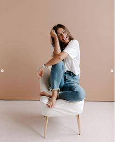 a woman sitting on top of a white chair with her hand on her head and smiling