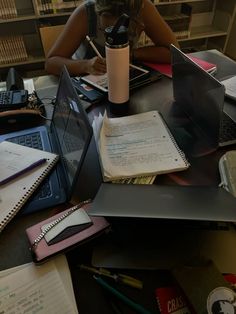 a woman sitting at a table with laptops and notebooks on top of it