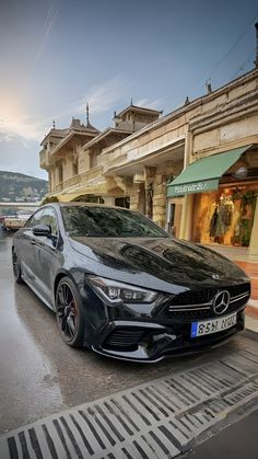 a black mercedes cla parked on the street in front of a building with shops