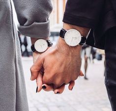 two people holding hands while standing next to each other on a brick sidewalk with buildings in the background