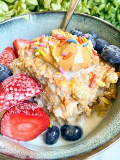 a bowl filled with oatmeal, strawberries and blueberries next to green leaves