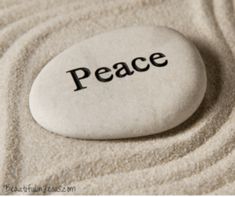 a white rock with the word peace written on it in black ink, surrounded by sand