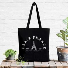 a black tote bag sitting on top of a wooden table next to potted plants